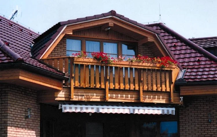 Dřevěný balkon s kvetoucími rostlinami na cihlovém domě.