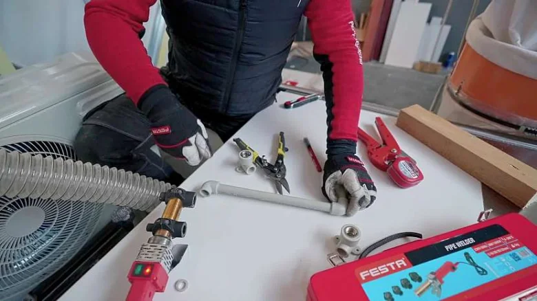 Ruce pracují na plastovém potrubí s nástroji pro domácí instalaci vody.