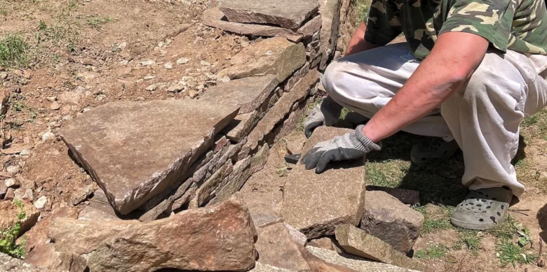 Muž staví kamennou zídku v zahradě rukama.