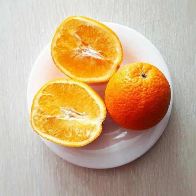 Bílý talíř s celým pomerančem a dvěma polovinami na dřevěném povrchu.