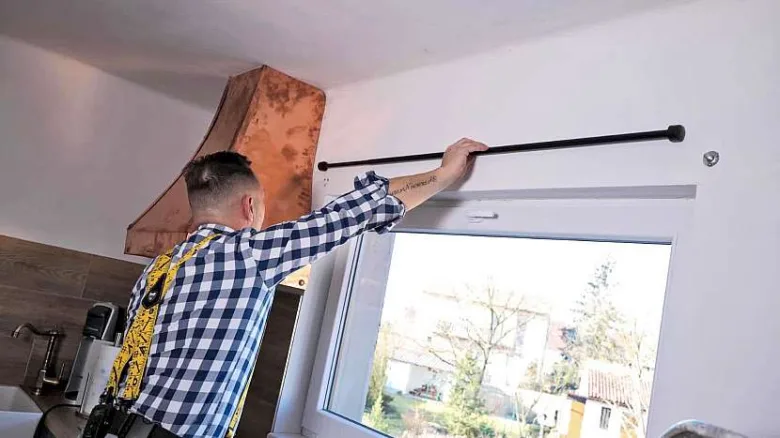 Muž montuje lištu pro závěsný roletu nad oknem.