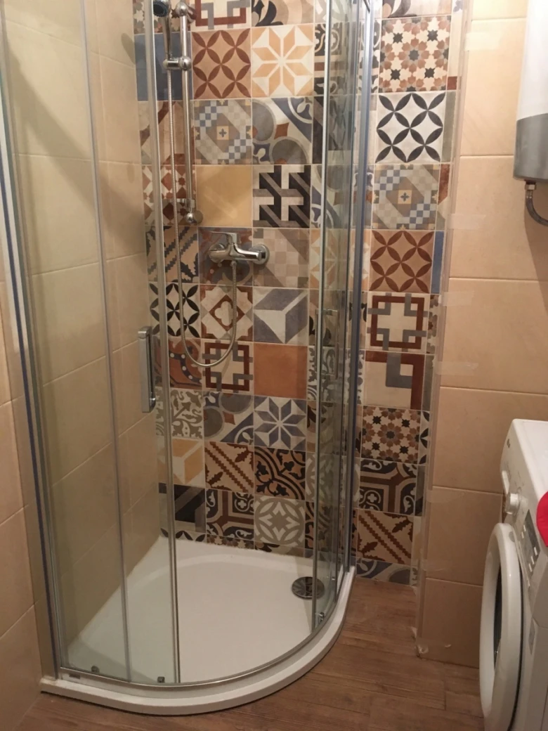 Dokončená renovace koupelny s barevnými dlaždicemi v sprchovém koutě.