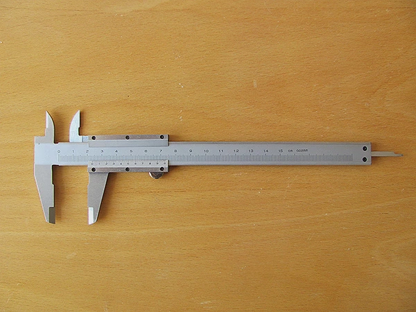 Stříbrná šuplera na světlém dřevěném povrchu pro měření.