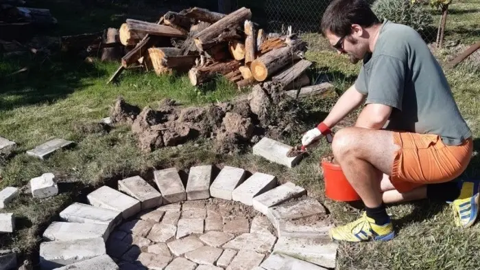 Muž staví kamenné ohniště na zahradě s dřevem.