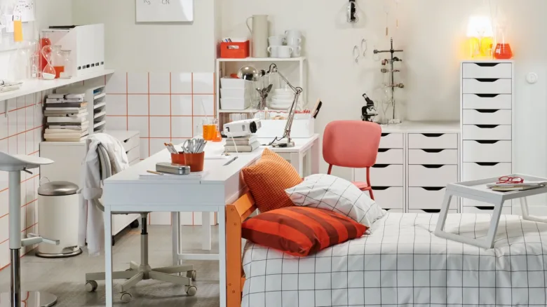 Organizovaný studentský pokoj s bílým nábytkem a oranžovými doplňky.
