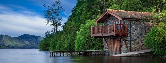 Kamenný dům s dřevěným balkonem nad jezerem.