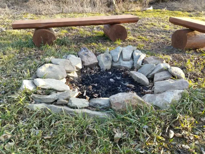 Přírodní ohniště v zahradě s dřevěnými lavičkami.
