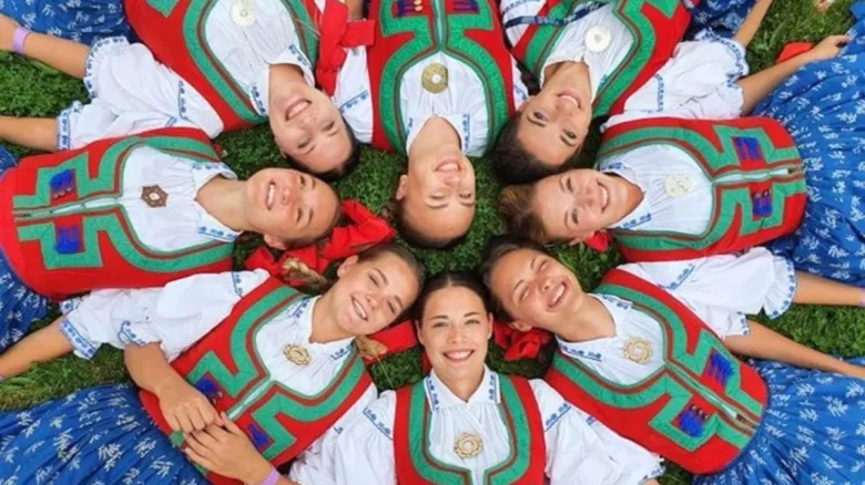 Ženy v valašských krojích leží na trávě ve kruhu.