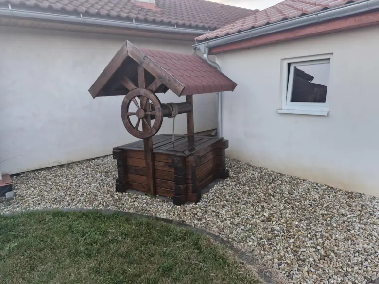 Dřevěná replika studně s čerpacím mechanismem na štěrku.