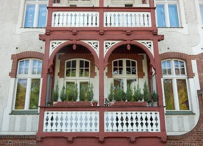 Detailní fotografie červeného dřevěného balkonu s květinami.