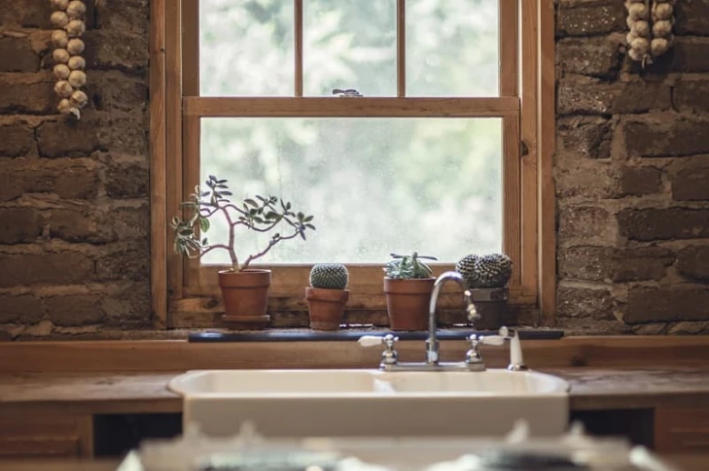 Opravené dřevěné okno v kuchyni s rostlinami.