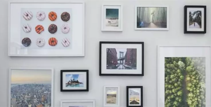 Různé rámované fotografie na bílé zdi galerie.
