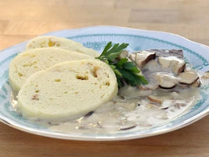 Přesnídané knedlíky s houbovou omáčkou na talíři.