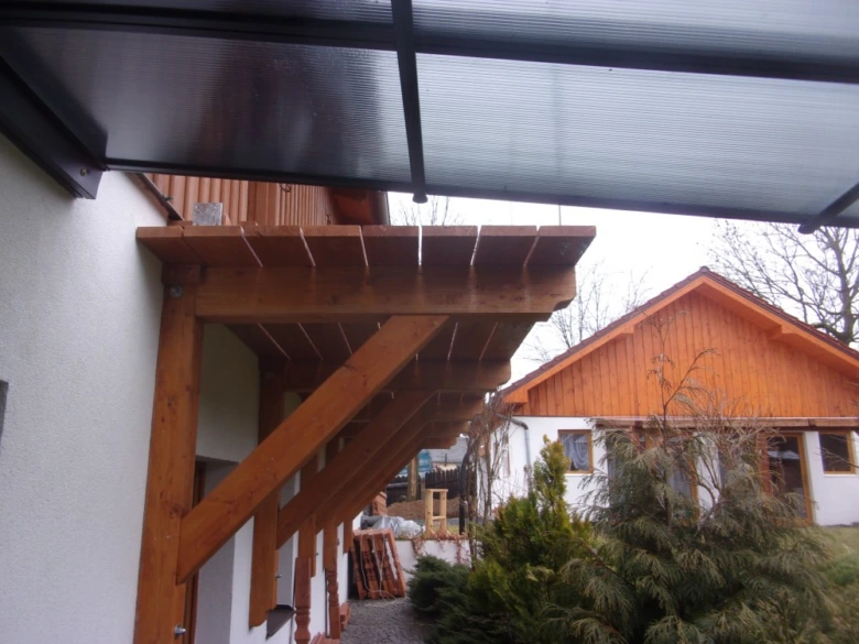 Dřevěný balkon s viditelnými nosnými prvky u domu.