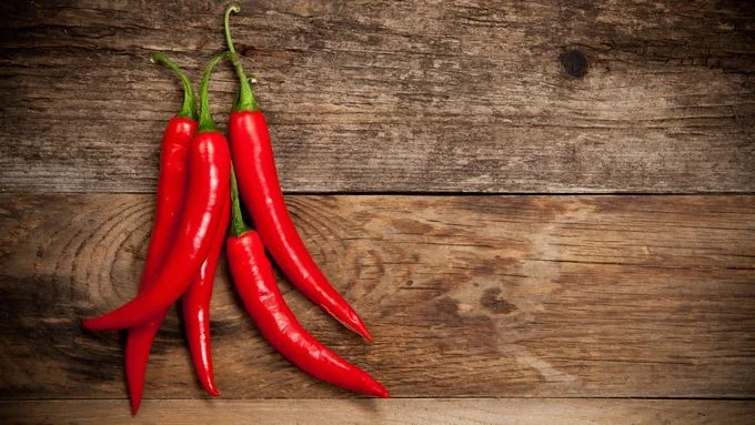 Červené chilli papričky na dřevěném povrchu.