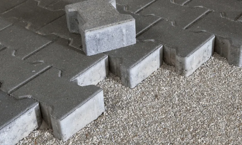 Šedé dlaždice na štěrkovém podkladu pro chodník kolem domu