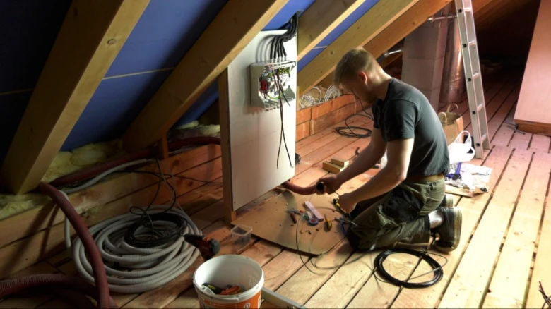 Elektrikář zapojuje fotovoltaický systém do rozvaděče v podkroví.
