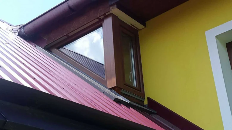 Střešní okno v žluté budově s červenou střechou.