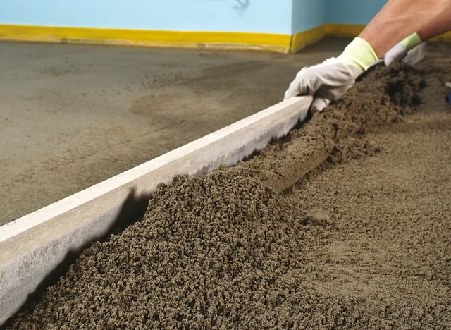 Pracovník vyrovnává čerstvý beton na podlaze.