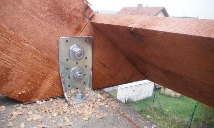 Kovová spojovací deska na dřevěném krovu s viditelnými šrouby.