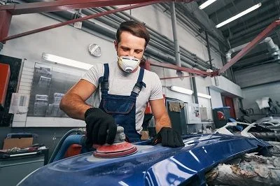 Autoklempíř šlifuje karoserii v dílně