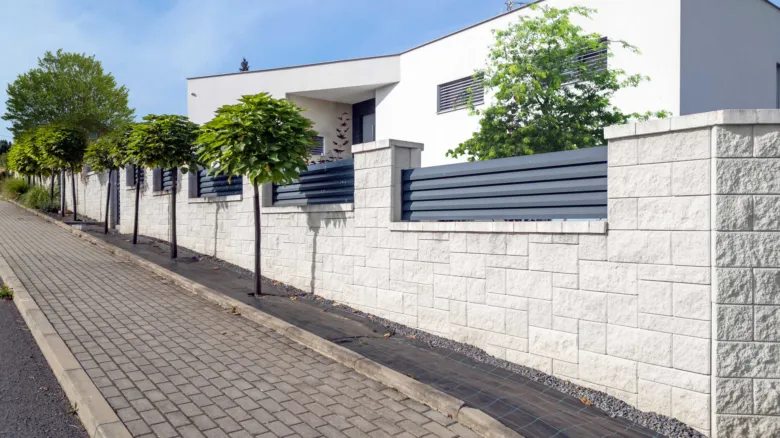 Modernní bílá zdi s tmavými lamelami tvořící část plotu.