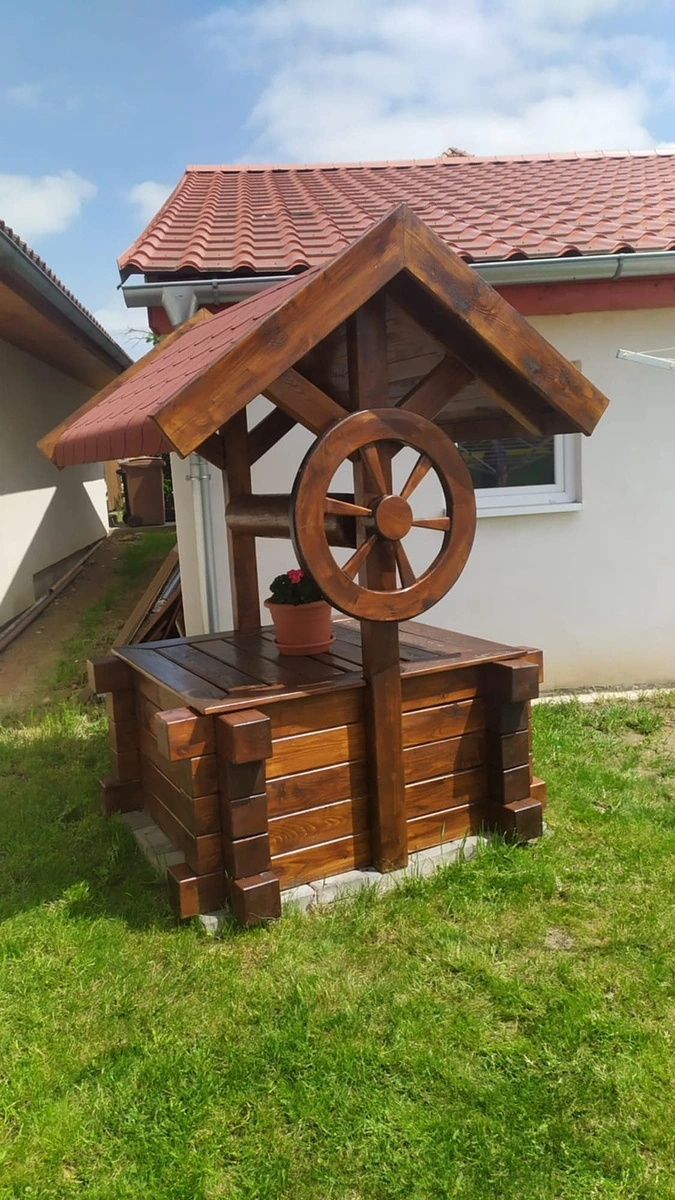 Dřevěná replika českého studně s koly a střechou na trávníku.
