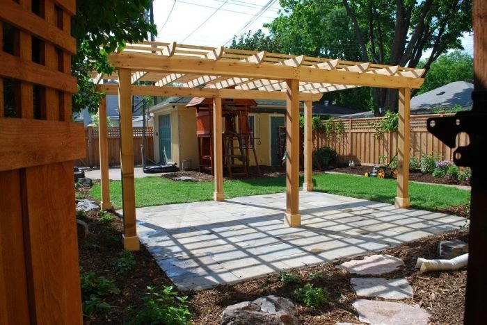Nově postavená dřevěná pergola nad kamennou terasou v zahradě.