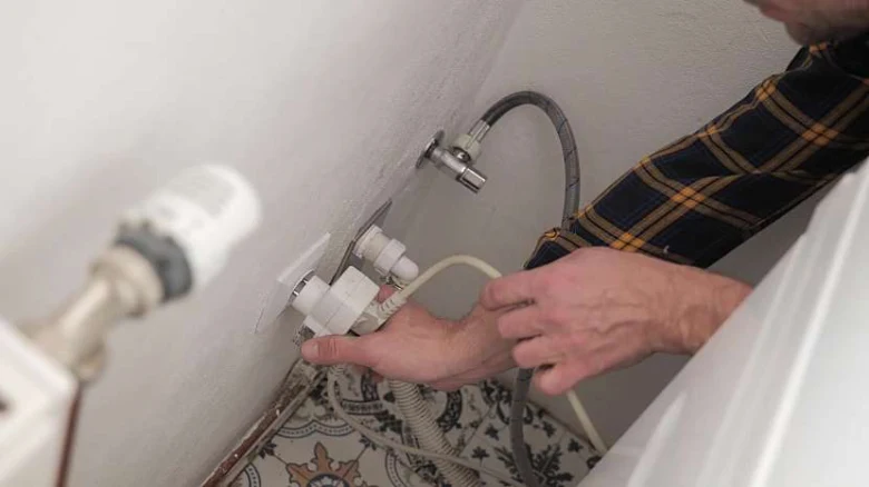 Muž připojuje hadice pračky k vodovodnímu kohoutku.