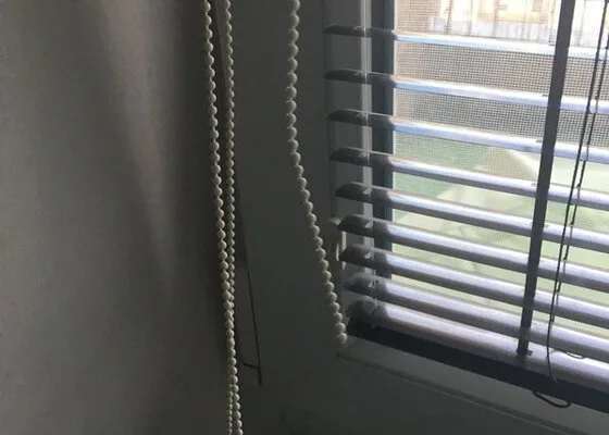 Bílé žaluzie u okna s táhly pro opravu v Plzni