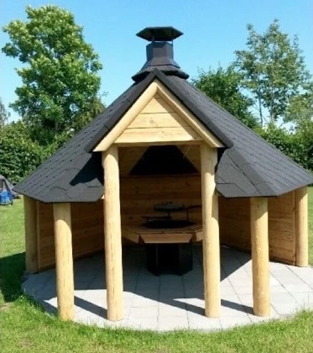 Dřevěný domek s komínem na trávníku pod modrou oblohou.