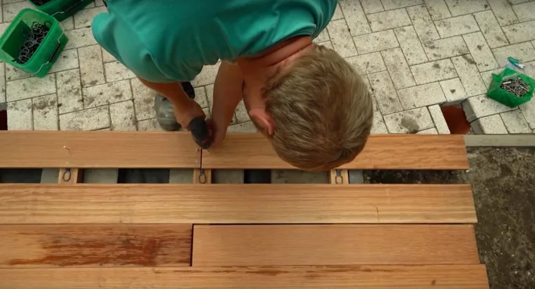 Muž staví dřevěnou terasu šroubovákem