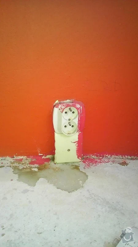 Poškozená elektrická zásuvka s odhalenými vodiči na oranžové stěně.
